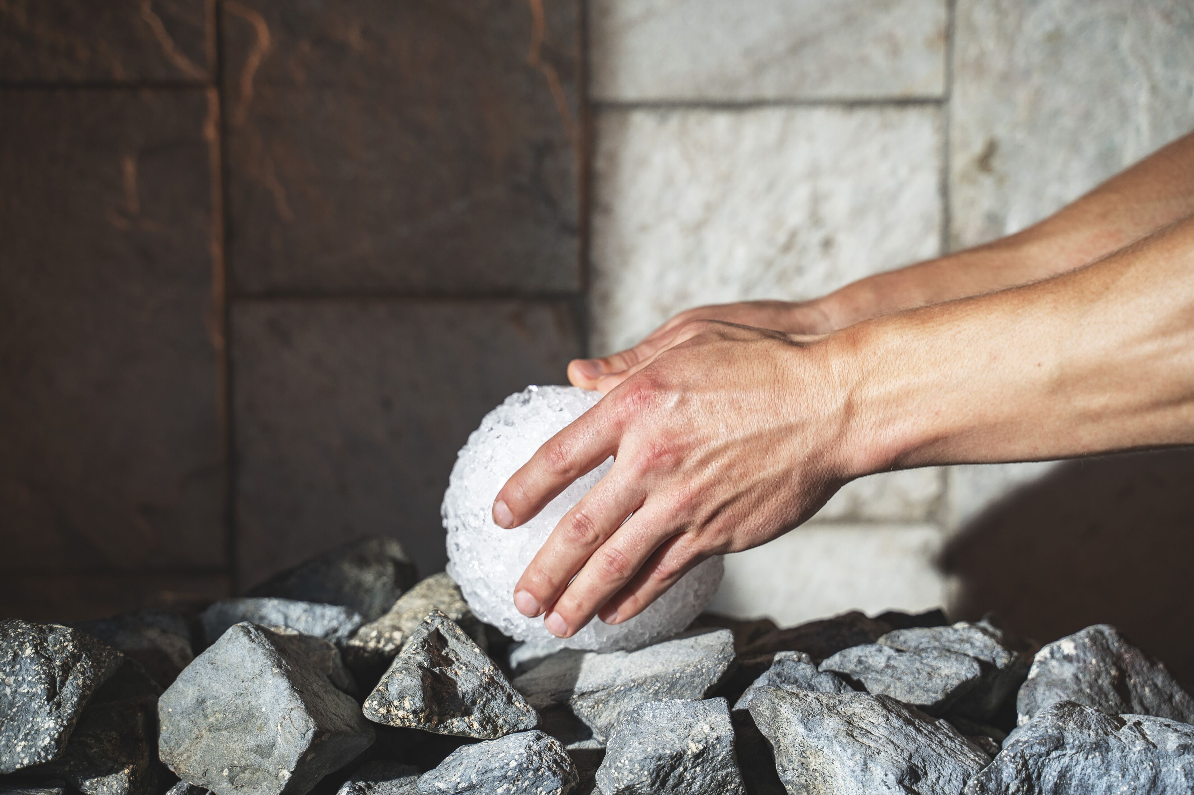 Hands placing a spherical object on a pile of rocks.