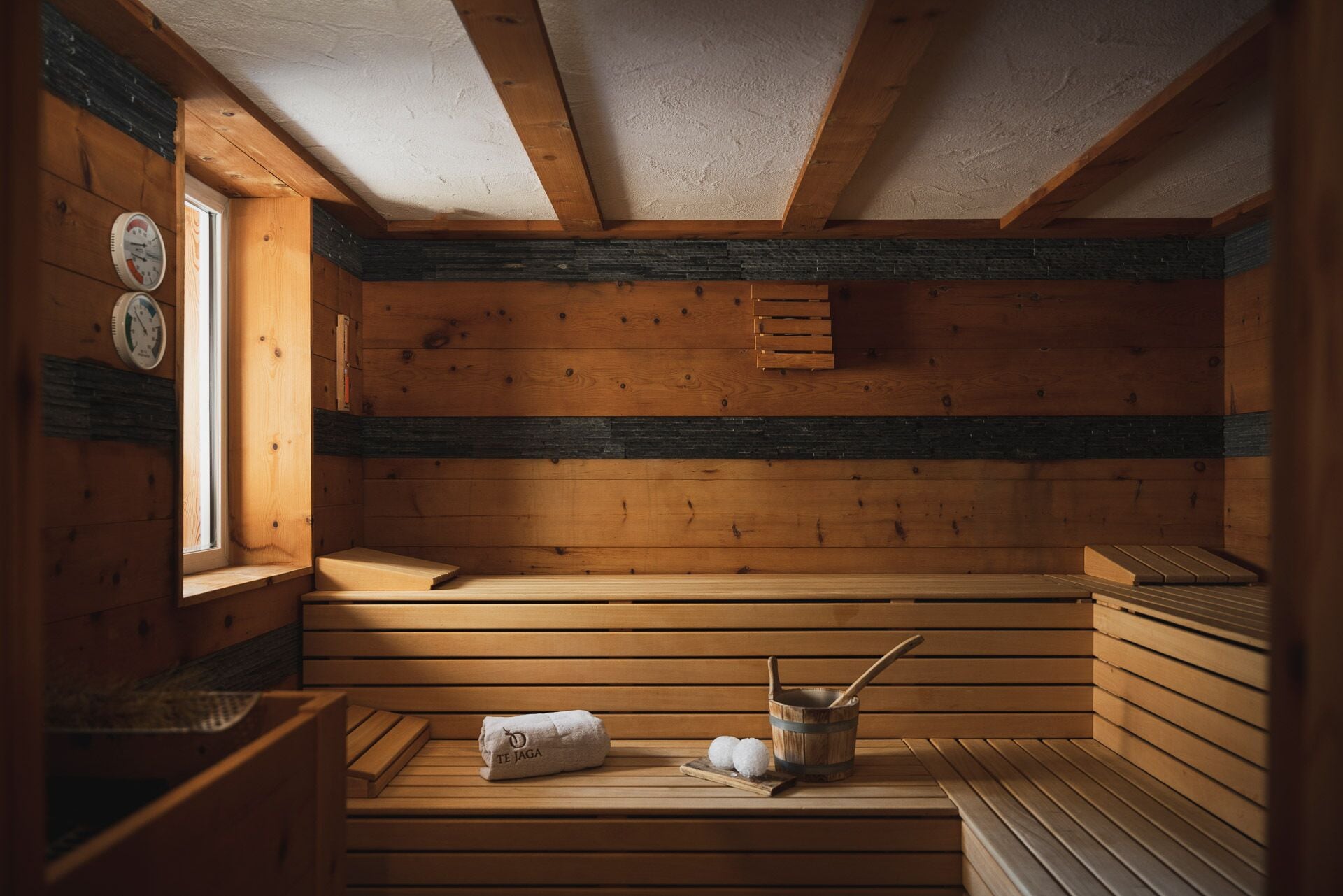 Un sauna avec des bancs en bois, un banc avec une serviette, un seau et une horloge murale.
