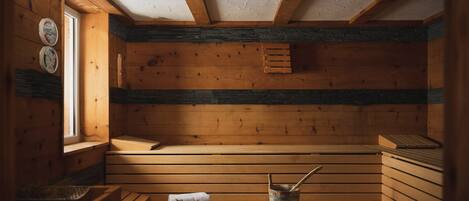 Un sauna avec des bancs en bois, un banc avec une serviette, un seau et une horloge murale.