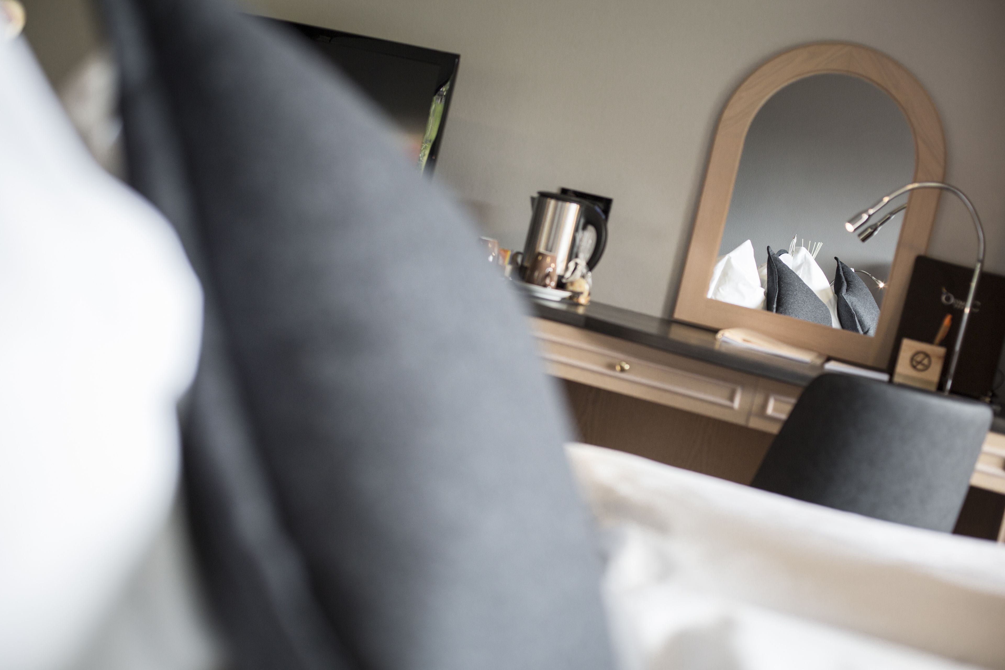 A hotel room with a bed, a bedside table, a mirror, and a coffee maker.