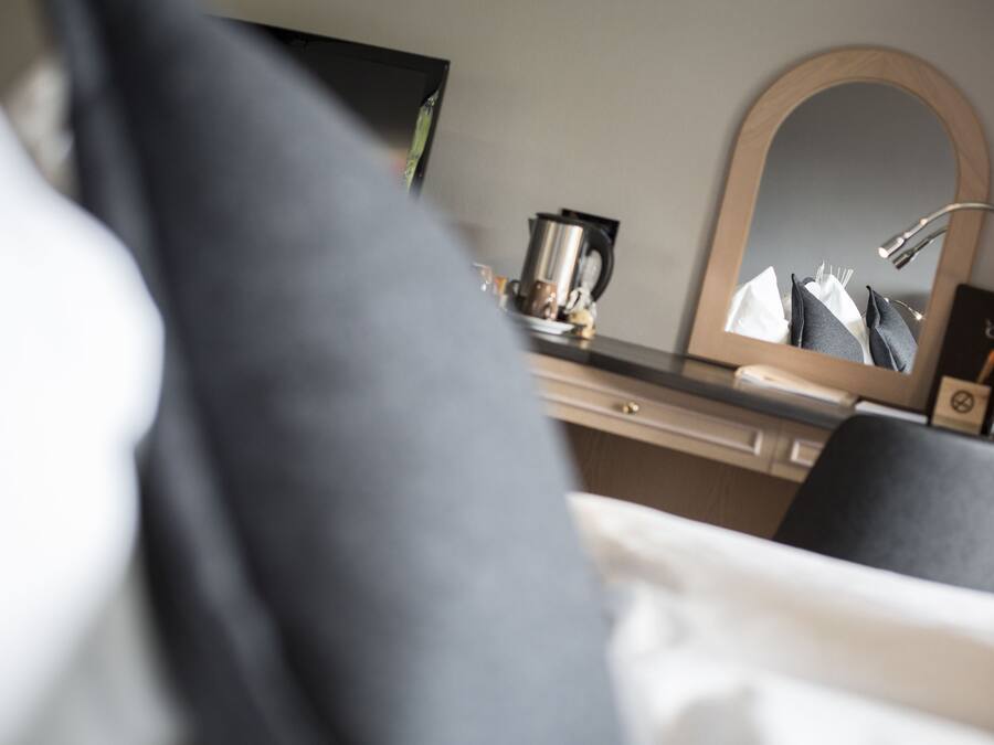 Una habitación de hotel con una cama, una mesita de noche, un espejo y una cafetera.