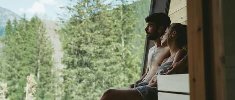 A couple sitting by a window overlooking a forested mountain area.