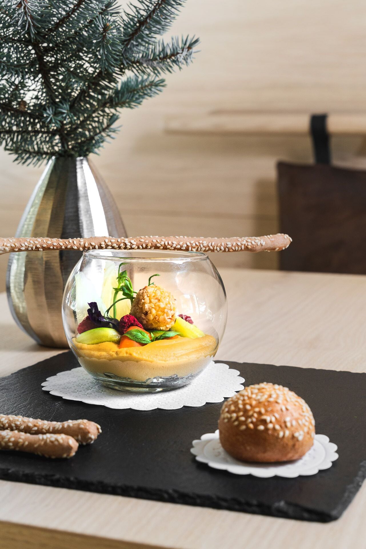 A dessert in a glass bowl on a black slate, with a small bun beside it.