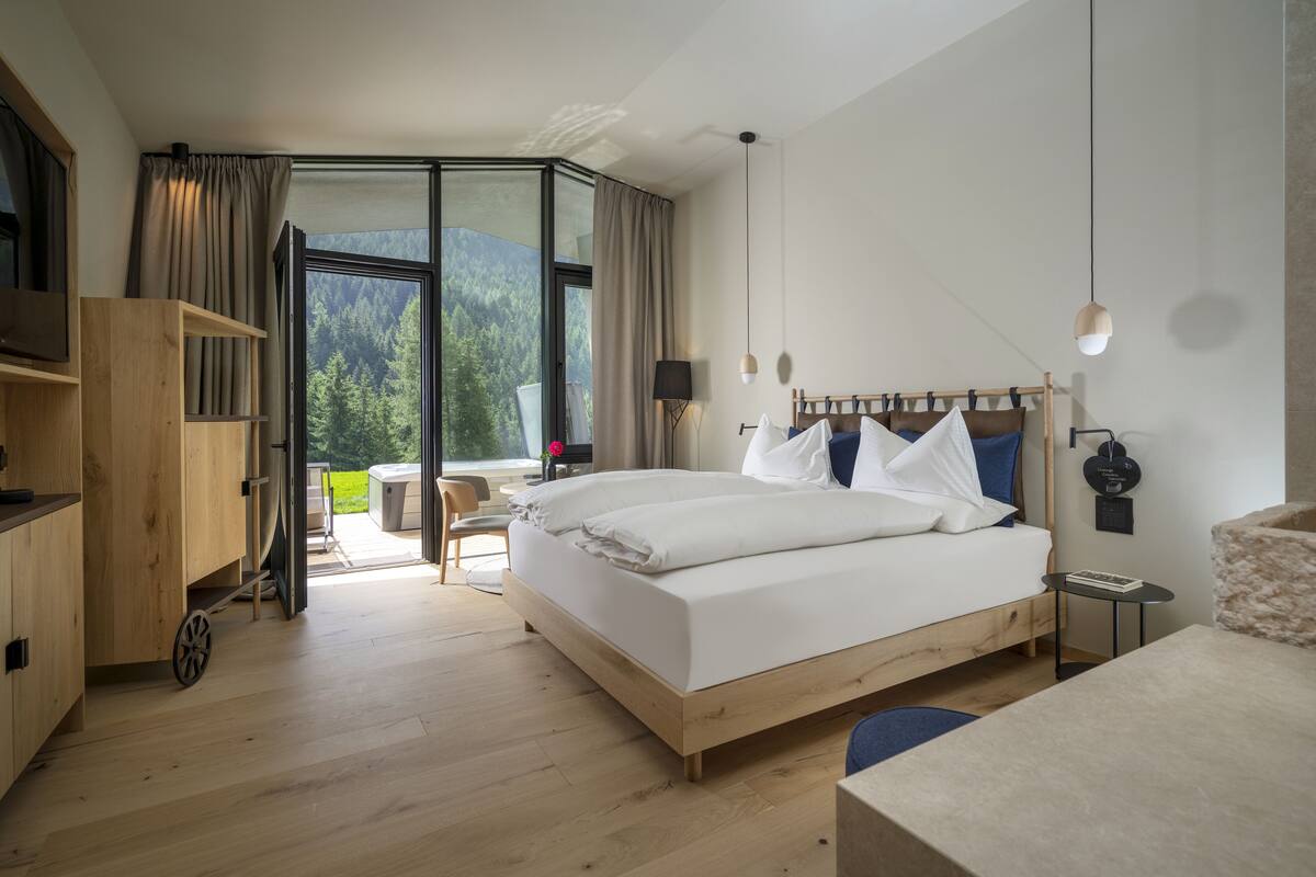 Un dormitorio moderno con una cama grande, un armario de madera, un escritorio y vistas a un bosque a través de una puerta de cristal.
