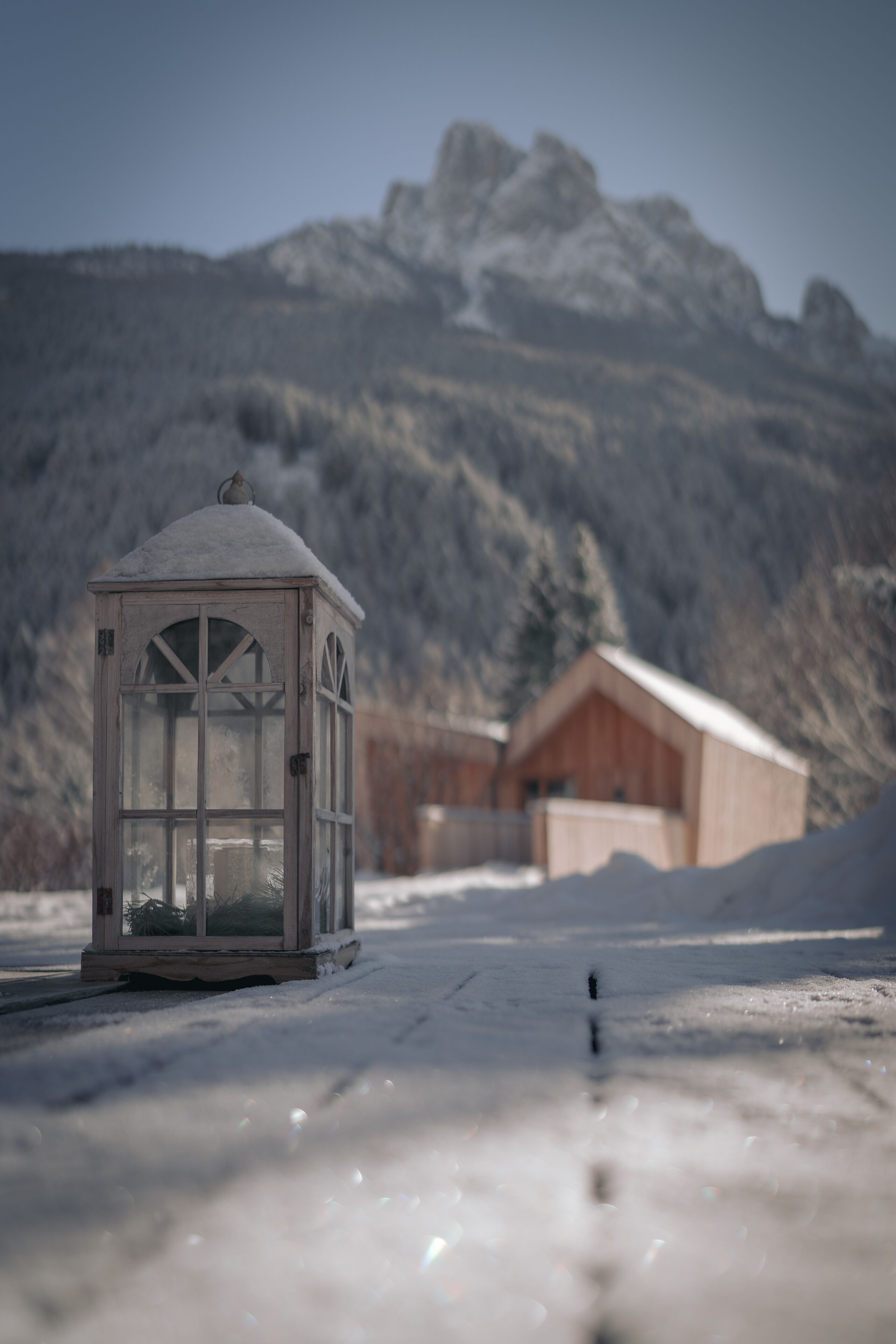 A snow-covered landscape with a wooden cabin and a glass structure in the foreground.