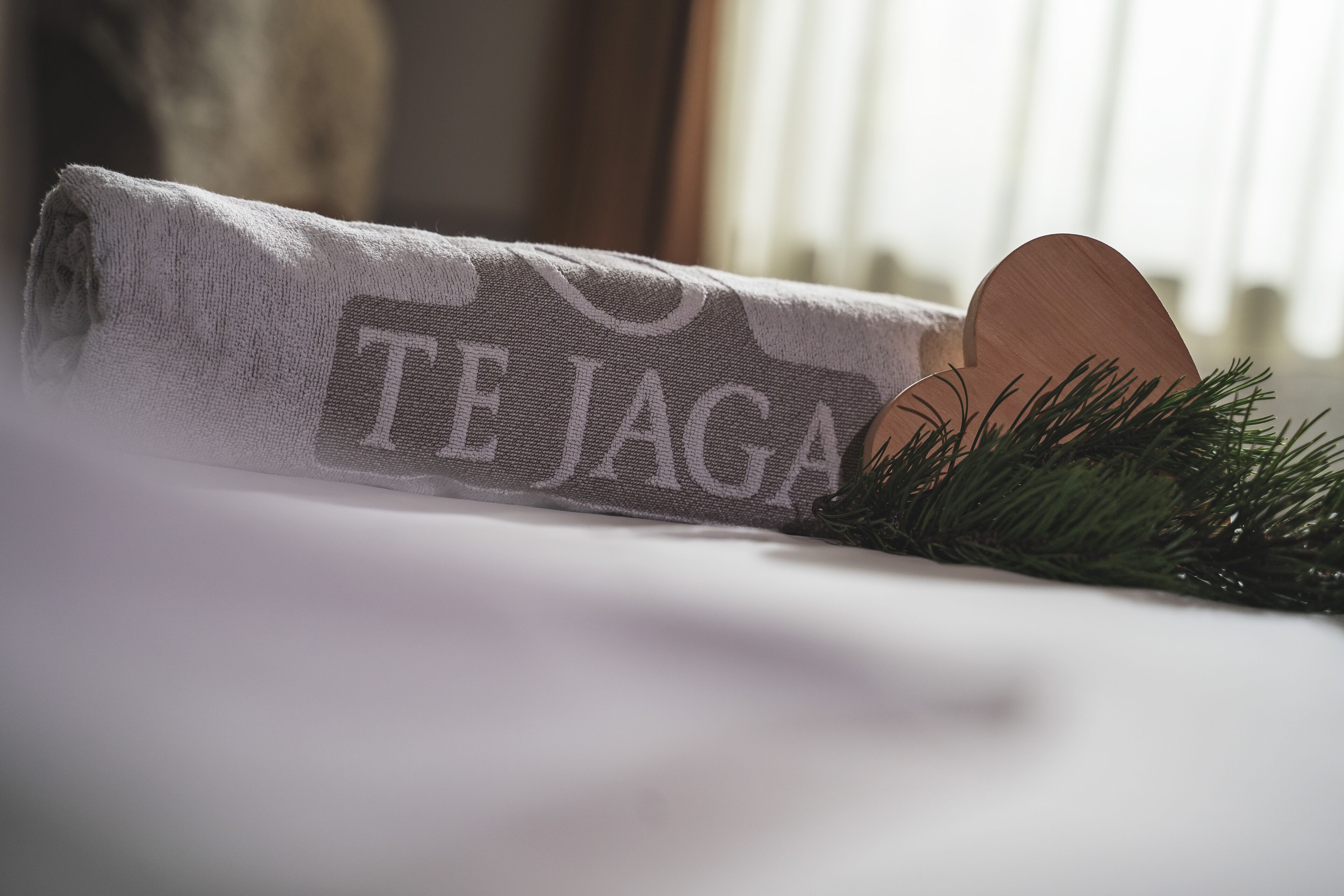 Een opgerolde handdoek met de tekst 'TE JAGA' en een houten object, mogelijk een dienblad, met groen ernaast.