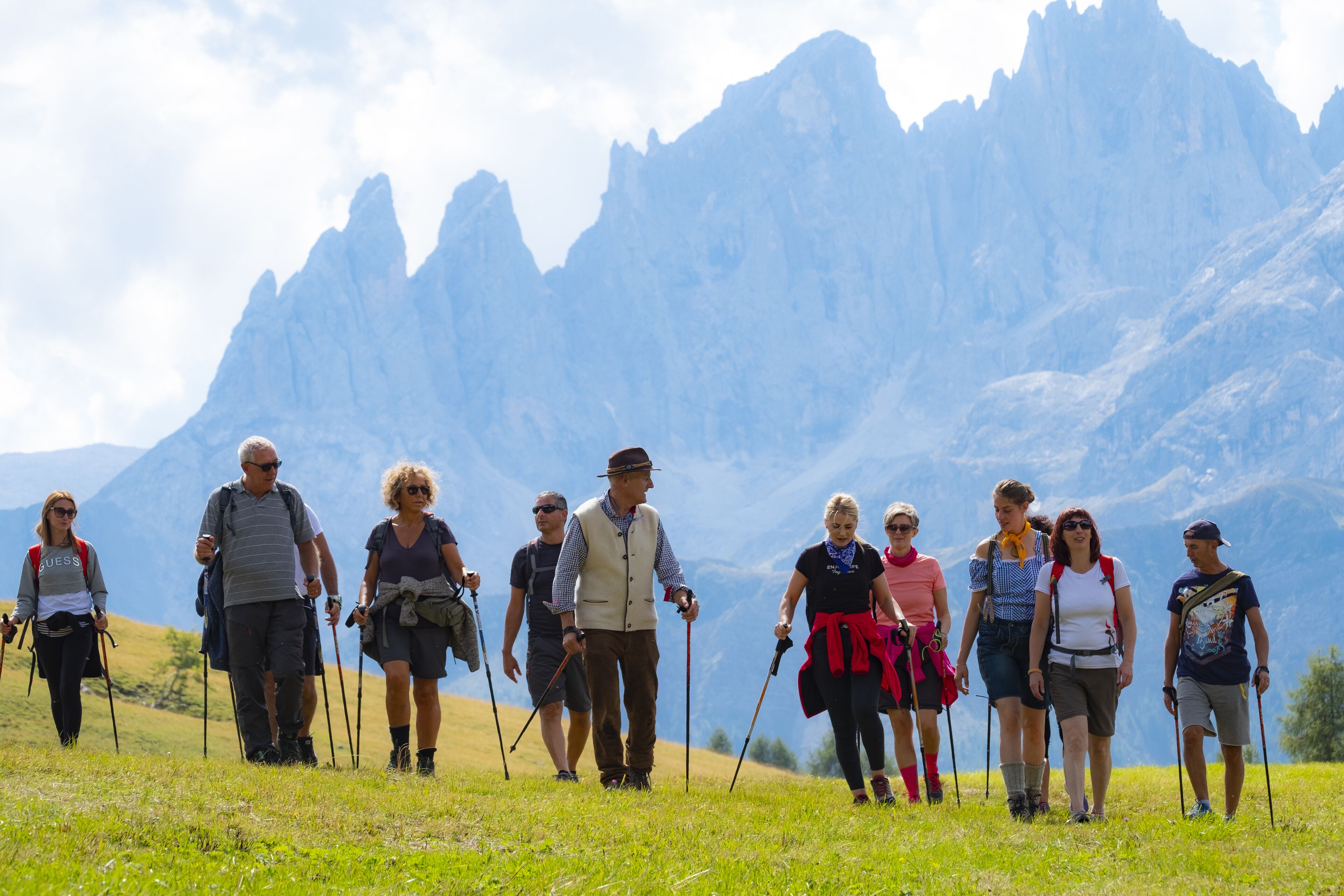 Un grupo de personas caminando por un sendero cubierto de hierba, con montañas al fondo.