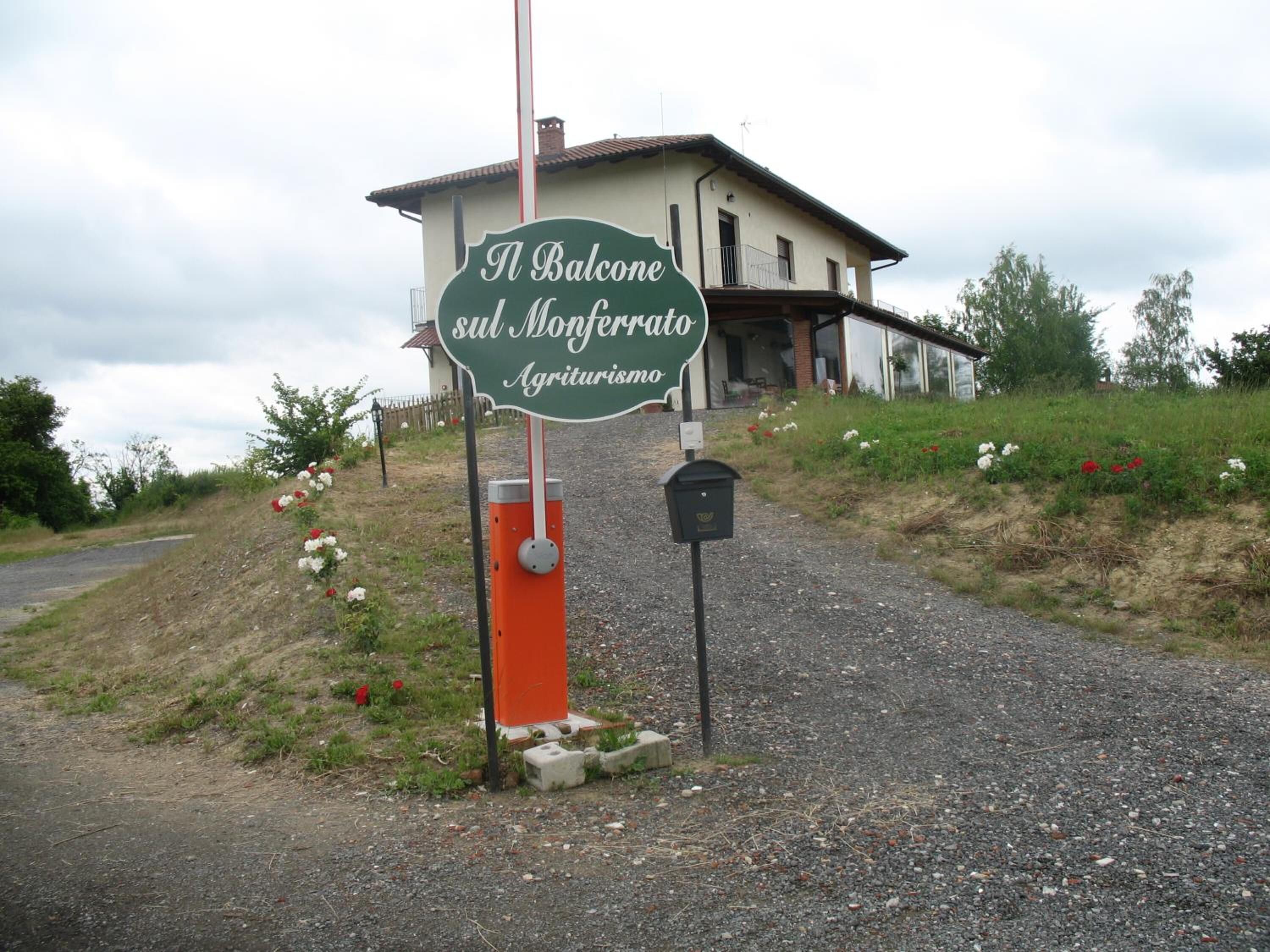 Une enseigne indiquant « A Balcone sul Monferrato Agriturismo », avec une maison en arrière-plan.