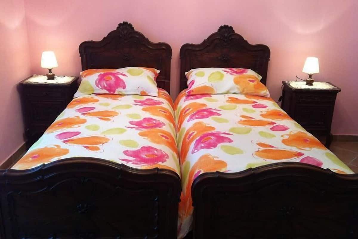 Two wooden beds with floral bedding, each with a bedside table and lamp.
