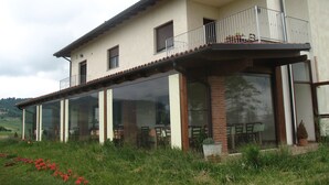 Una casa de dos pisos con balcón, amplias ventanas y un área verde con flores.