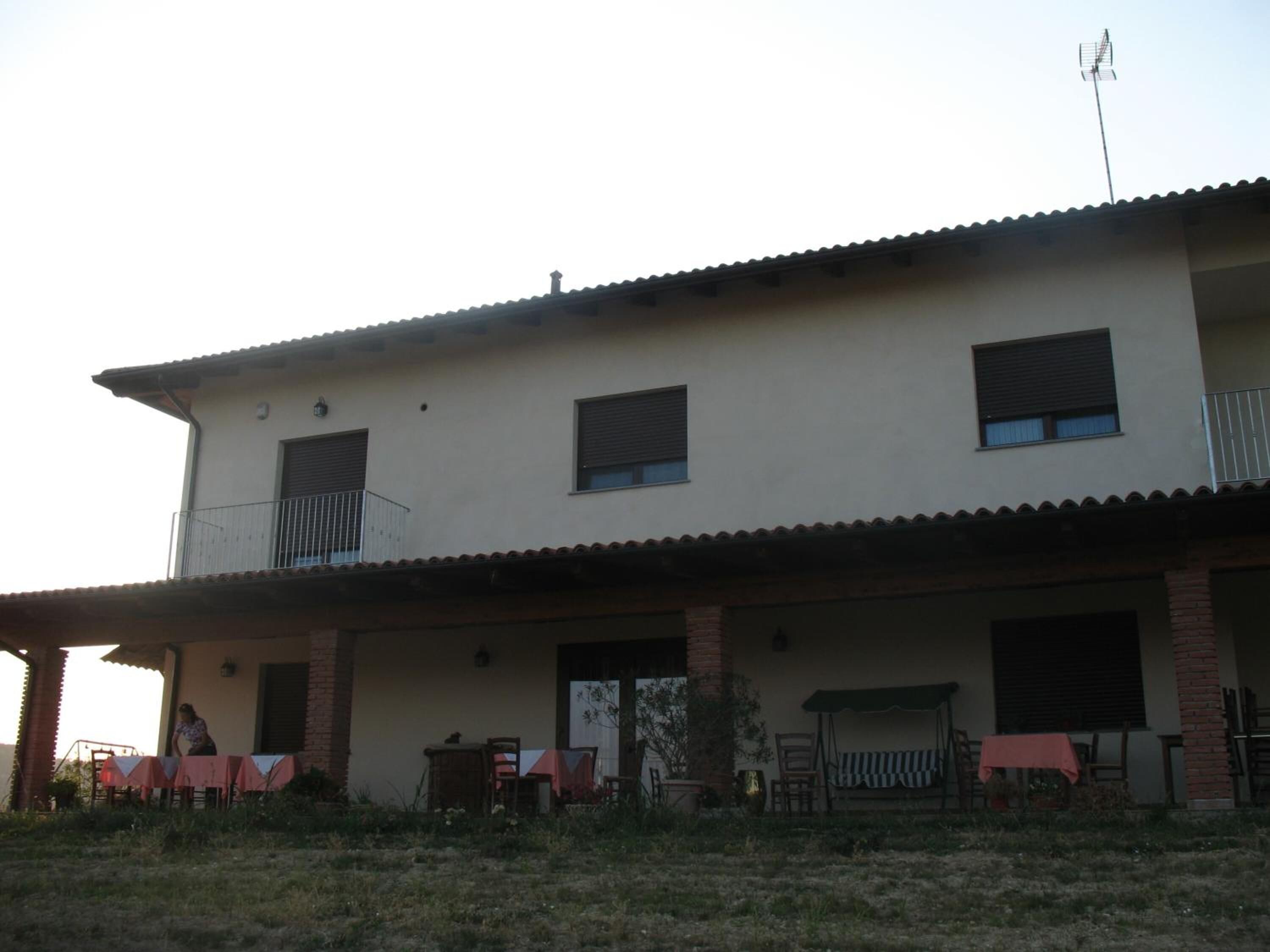 A two-story building with a flat roof, a balcony on the second floor, and a covered outdoor seating area with tables and chairs.