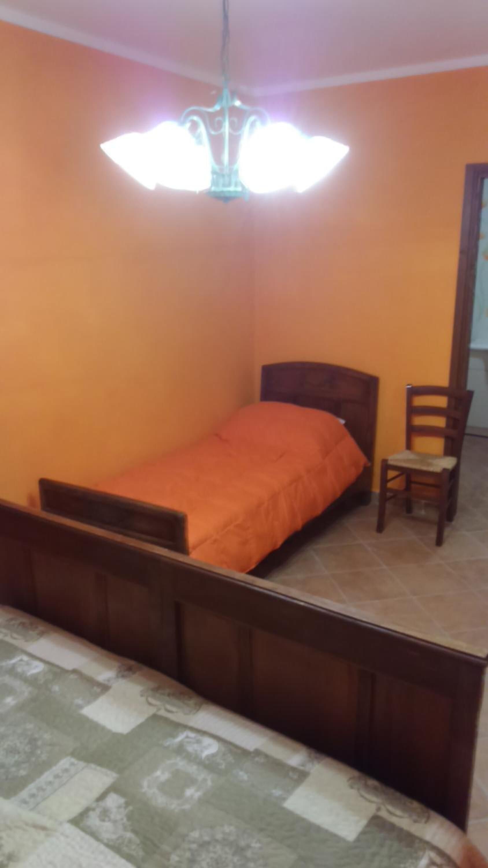 A bedroom with a single bed, a wooden chair, and a ceiling light fixture.