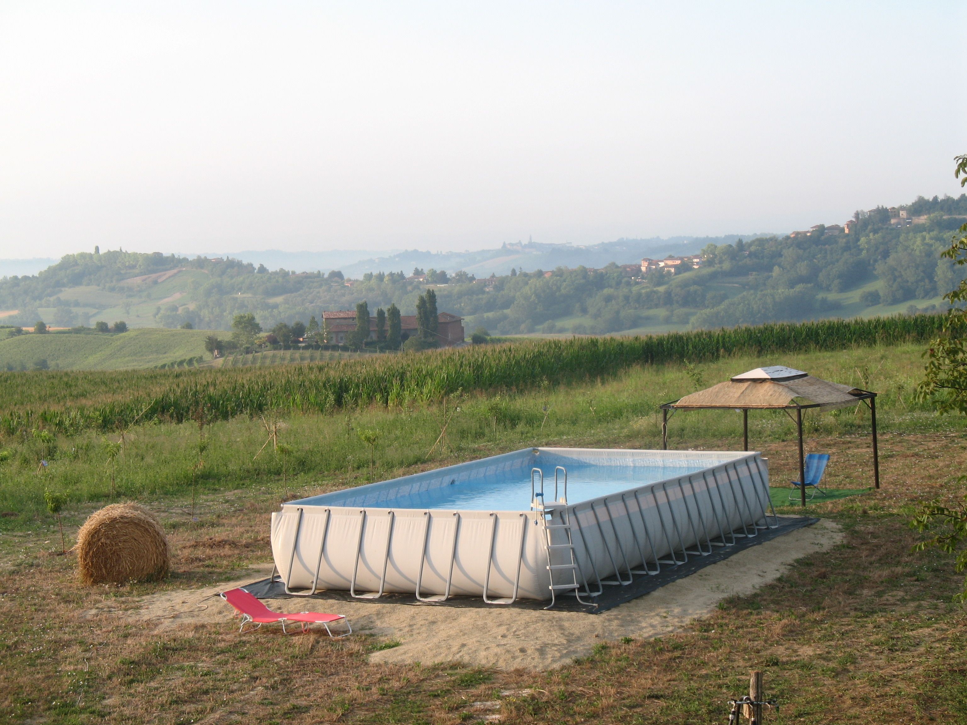 A rectangular swimming pool with a ladder, a red lounge chair, and a shaded area with a thatched roof.
