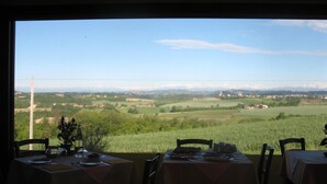 Un área de comedor con mesas preparadas para dos, con vistas a un paisaje pintoresco con campos y montañas al lejano.