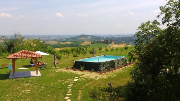 Una piscina rodeada por un jardín con un pabellón y vistas al campo.