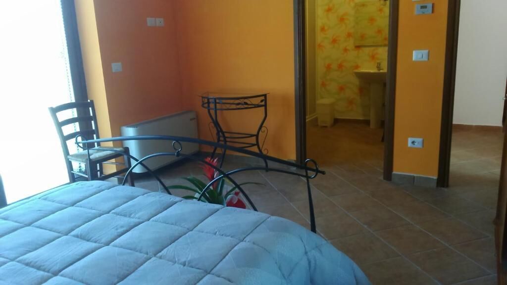 A bedroom with a bed, a chair, a small table, and a view of a bathroom.
