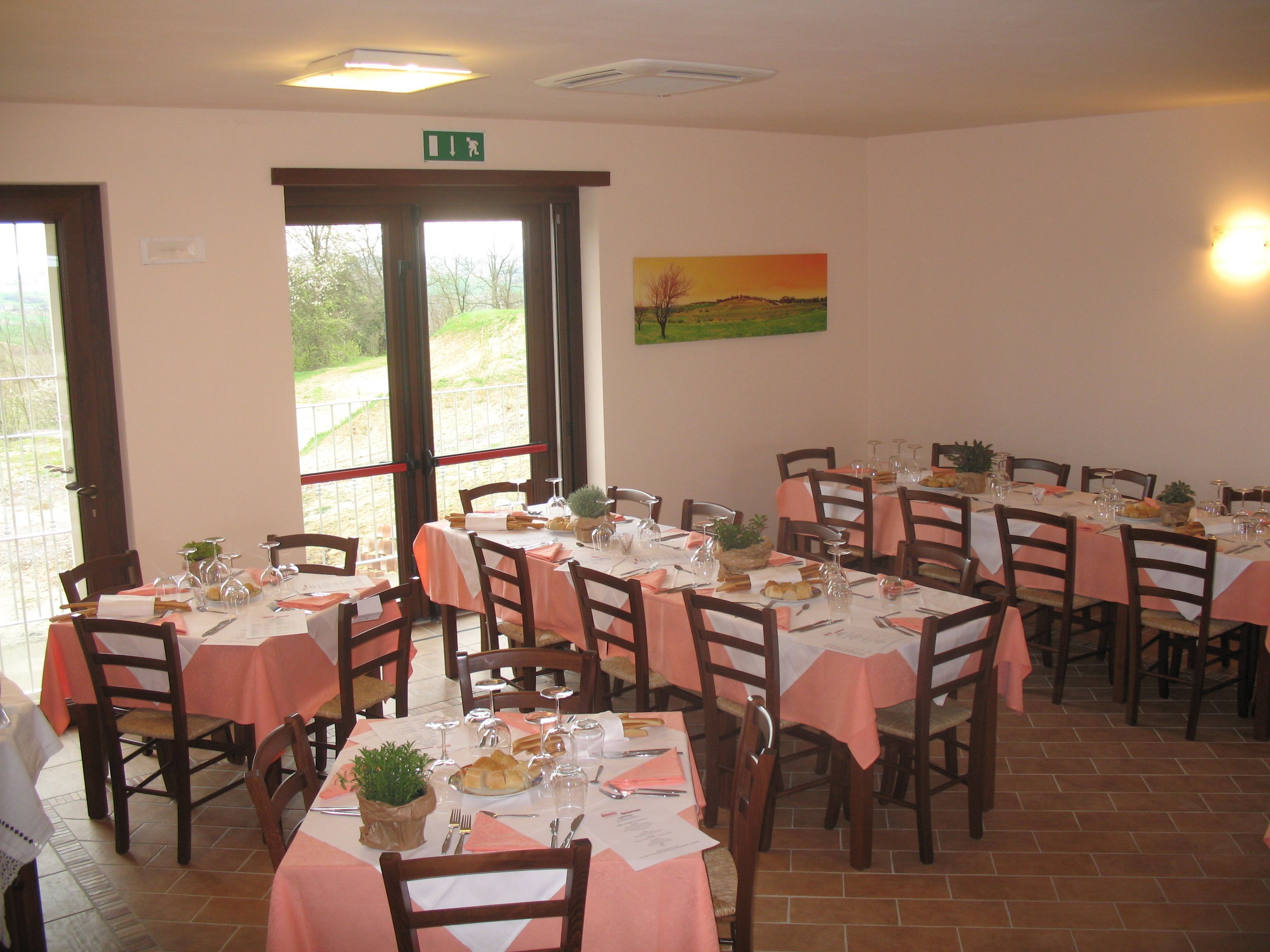 A restaurant with multiple tables set for dining, featuring a view of the outdoors through large windows.