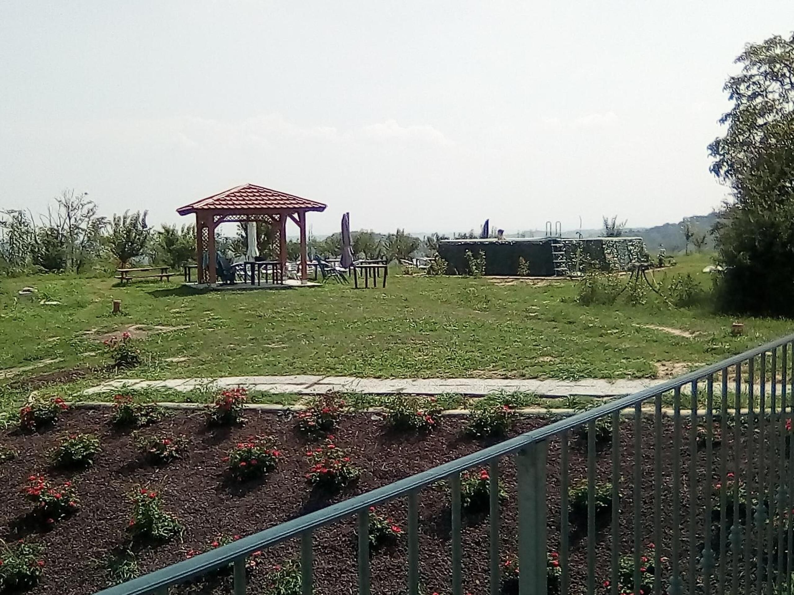 Ein Gazebo mit einem Ziegeldach, umgeben von einer Rasenfläche mit vereinzelten Stühlen und Tischen.