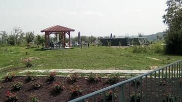 Ein Gazebo mit einem Ziegeldach, umgeben von einer Rasenfläche mit vereinzelten Stühlen und Tischen.