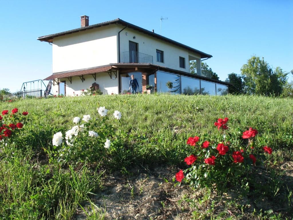A two-story house with a balcony, surrounded by a grassy field with red and white flowers.