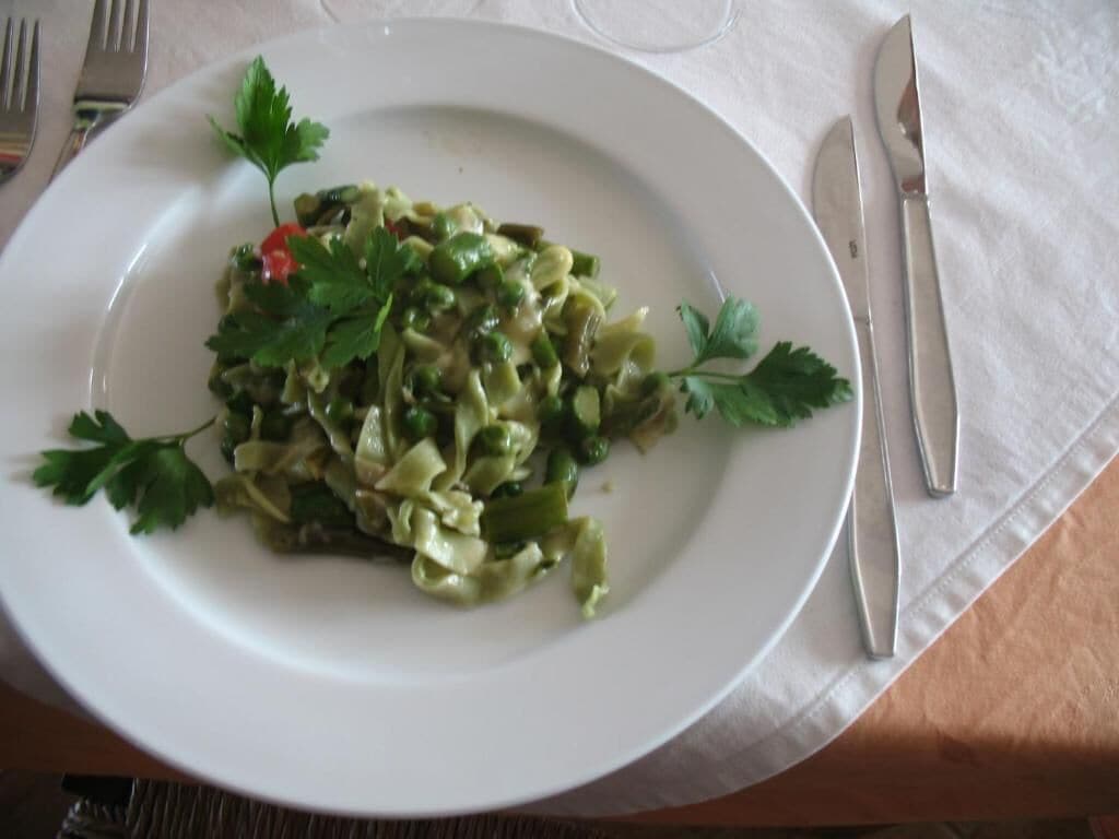 A plate of pasta with a garnish on a white plate, placed on a table with a white tablecloth.