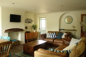 A living room with a brown leather sofa, wooden coffee table, and a TV mounted on the wall. - Mousetrap (Wells-next-the-Sea)