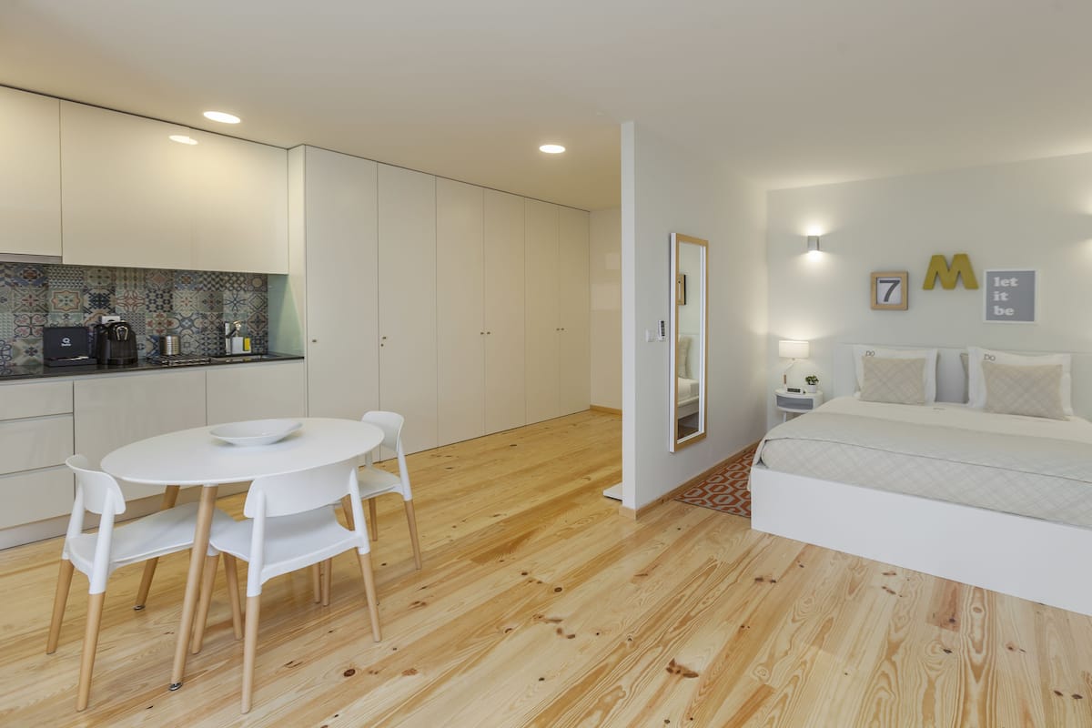 Une chambre moderne avec un grand lit, une table de chevet et une commode. Il y a un petit coin cuisine équipé d’un évier, d’une cuisinière et de placards.