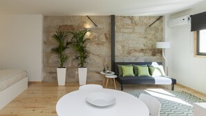 A modern living room with a stone wall, a sofa with green cushions, a white table, and a potted plant. - Oporto Local Studios (Porto)