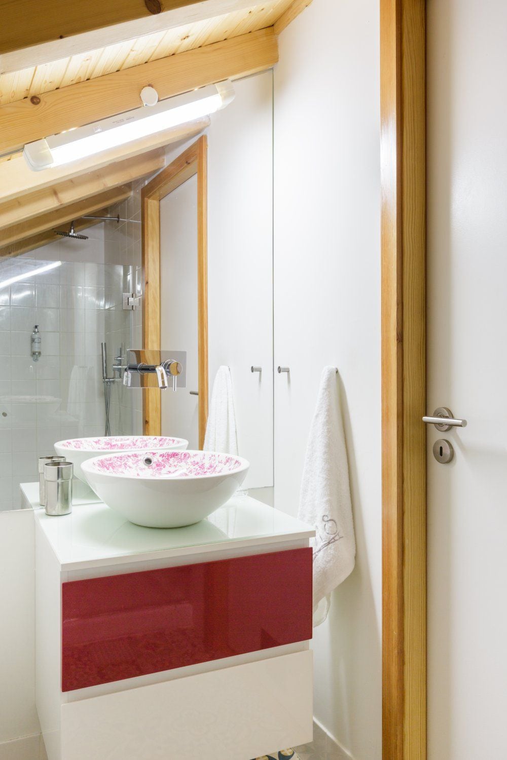 A bathroom with a white vanity, two pink floral sinks, a glass shower enclosure, and a wooden ceiling.