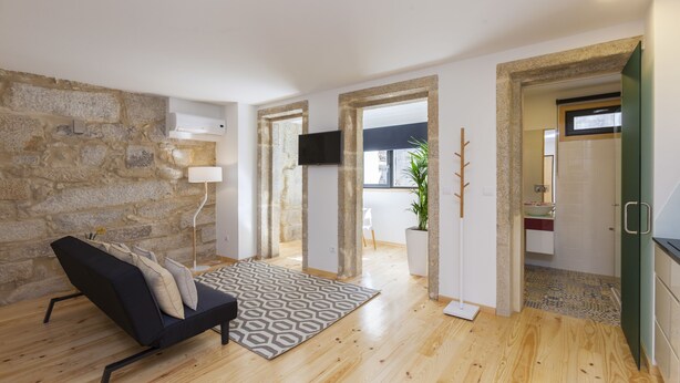 A modern living room with a stone wall, a black sofa, a patterned rug, and a wooden floor. - Oporto Local Studios (Porto)