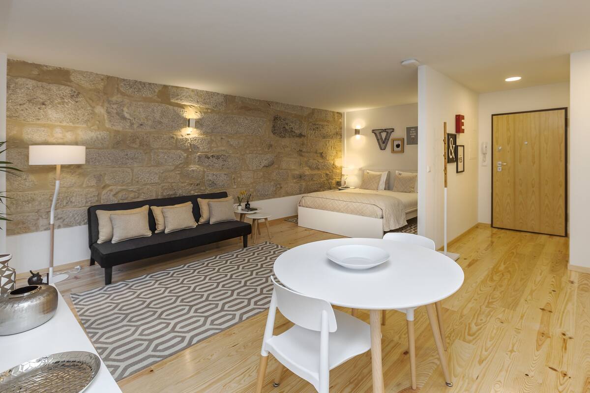 Un salon moderne avec un mur en pierre, un canapé noir, une table à manger blanche et un plancher en bois.
