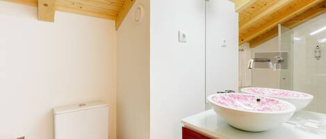 Un baño con vigas de madera, paredes blancas, una encimera roja y dos lavamanos blancos con motivos florales rosados.