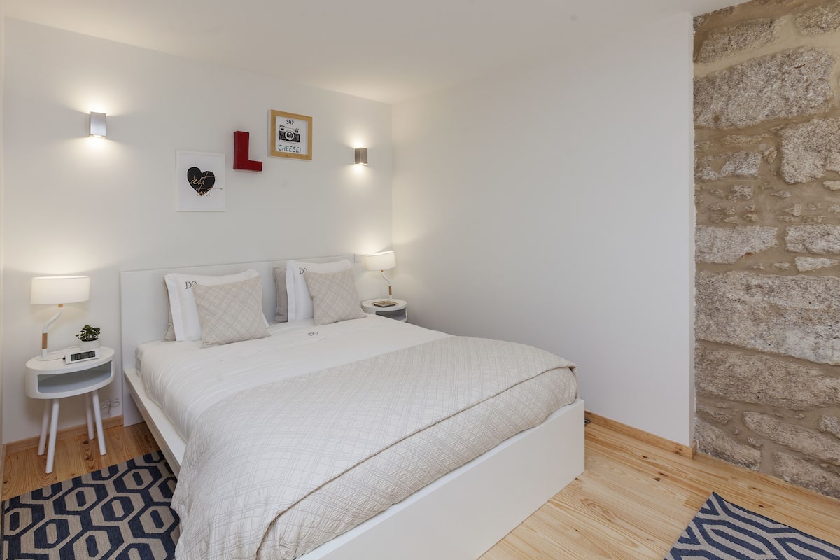 Une chambre bien rangée, avec un lit, des tables de chevet et un luminaire fixé au mur.