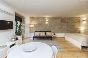 Una sala de estar moderna con una pared de acento de piedra, un sofá negro, una mesa de comedor blanca y una cama blanca.