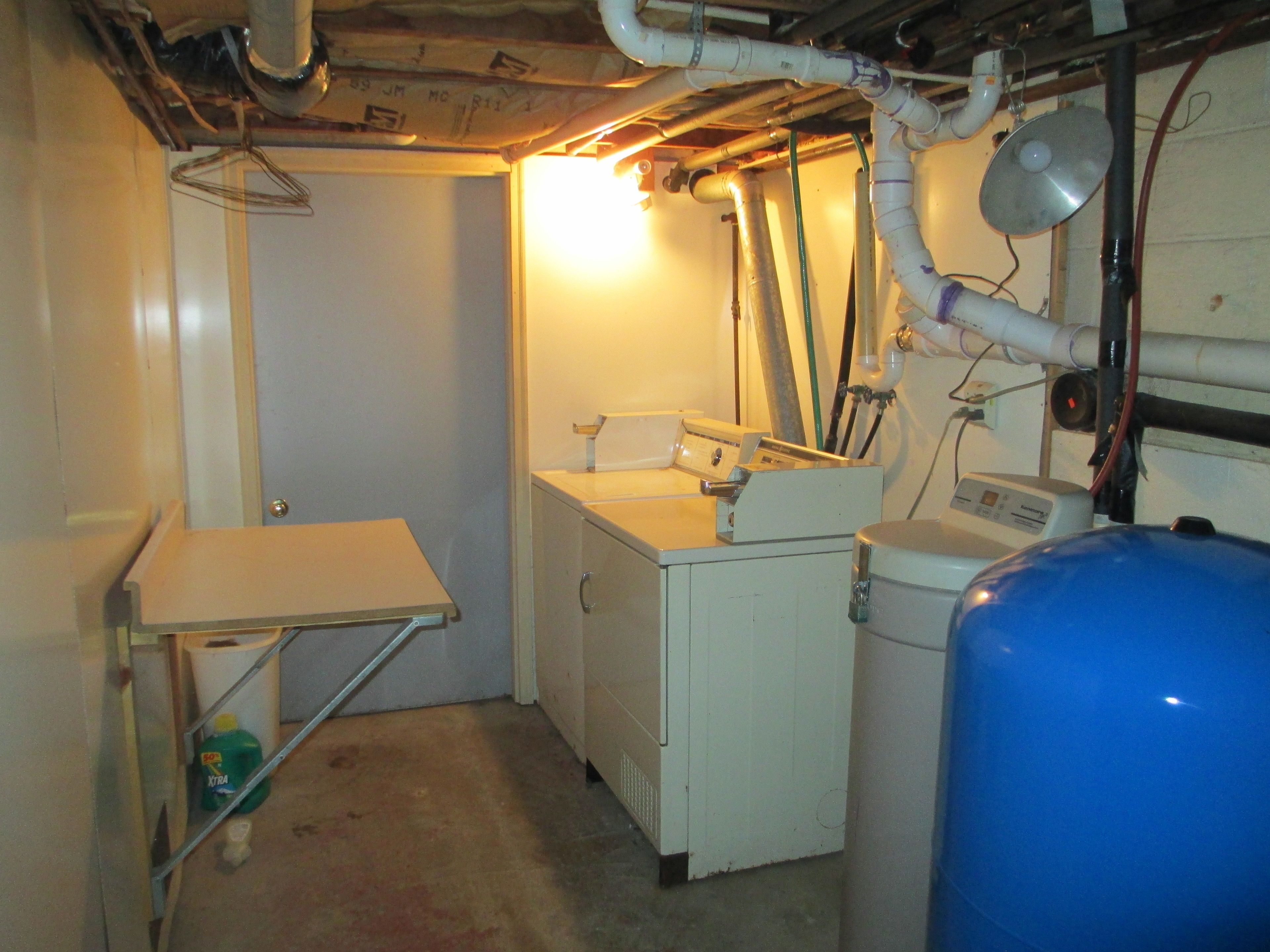 A small, industrial-style room with a sink, a washing machine, and a large blue water tank.