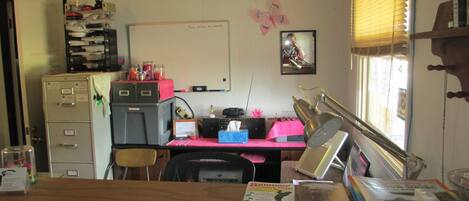 A small office with a desk, filing cabinets, a whiteboard, and a window with blinds.