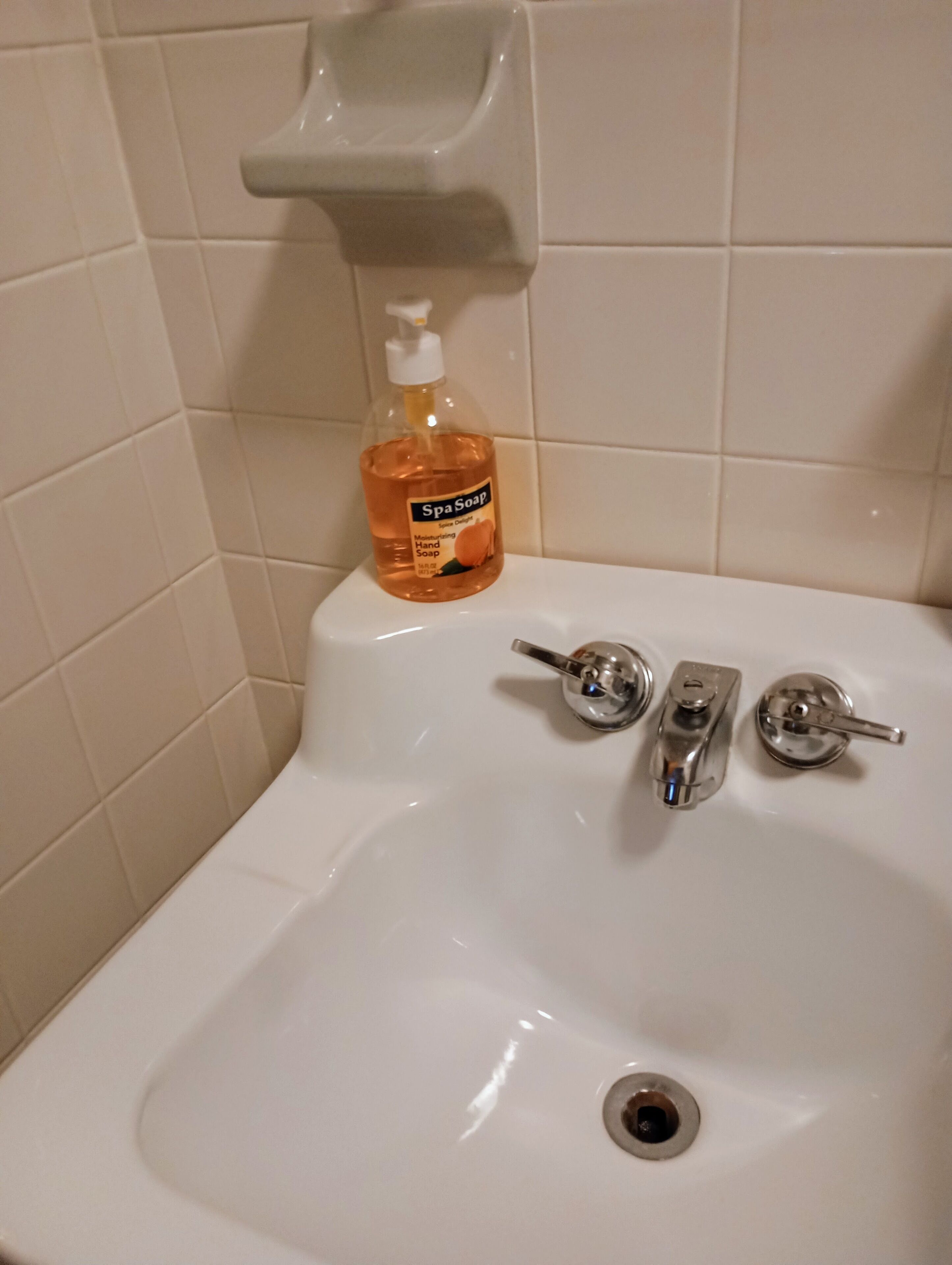 A bathroom sink with a hand soap dispenser, a faucet, and a drain.