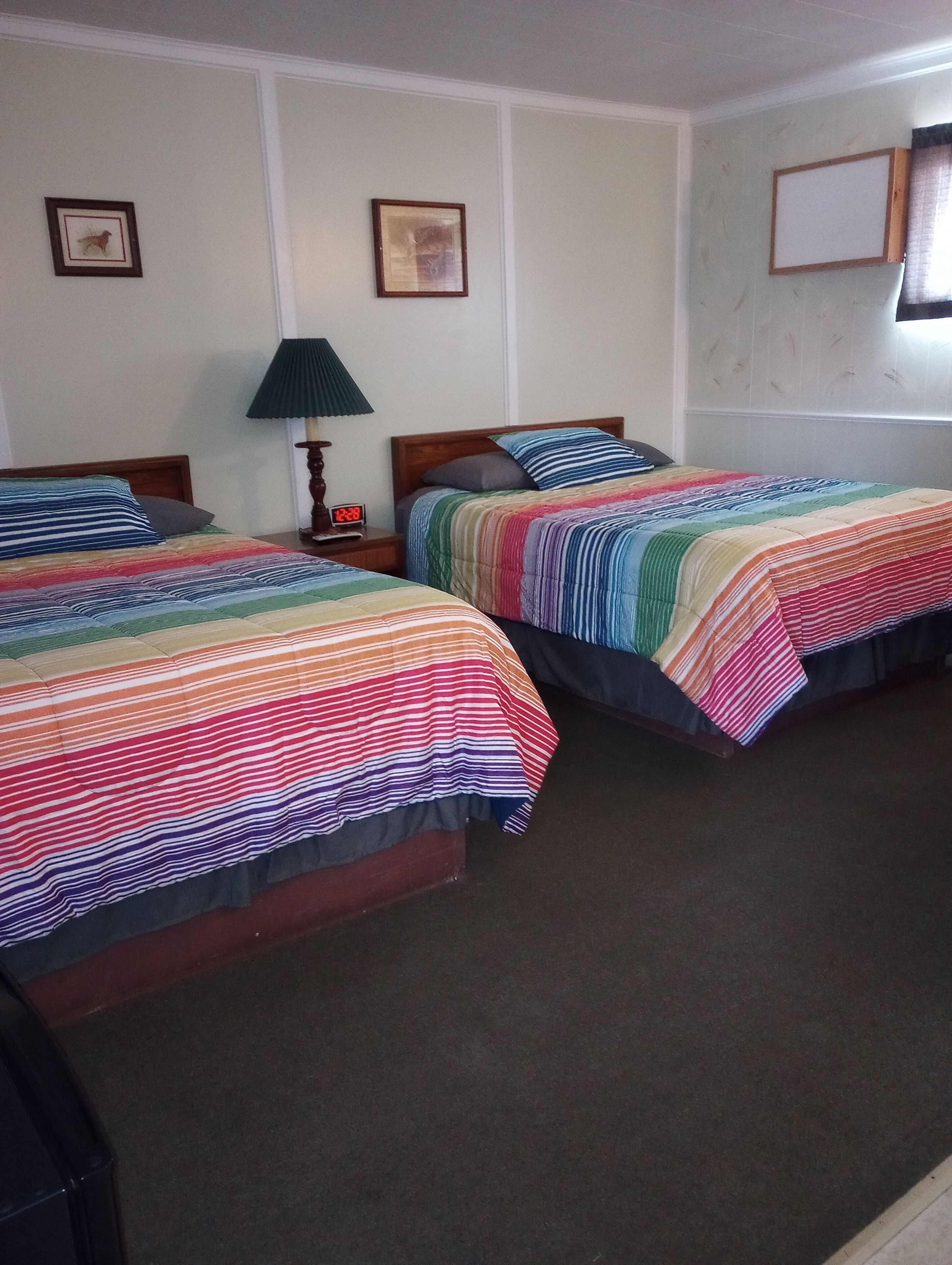 A hotel room with two single beds, a nightstand with a lamp, and a wall clock.