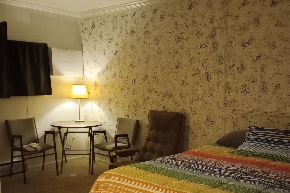 A hotel room with a bed, two chairs, a small table, and a lamp.