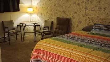 Ein Hotelzimmer mit einem Bett, zwei Stühlen, einem kleinen Tisch und einer Lampe.
