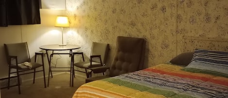 A hotel room with a bed, two chairs, a small table, and a lamp.