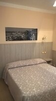 Een hotelkamer met een bed, een aan de muur bevestigd schilderij en een klein plankje met twee voorwerpen.