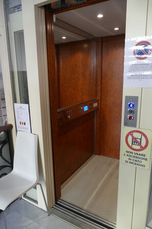 An elevator interior with a control panel, a sign indicating no use in case of fire, and a bar menu on the wall. - Hotel Cantore (Genoa)