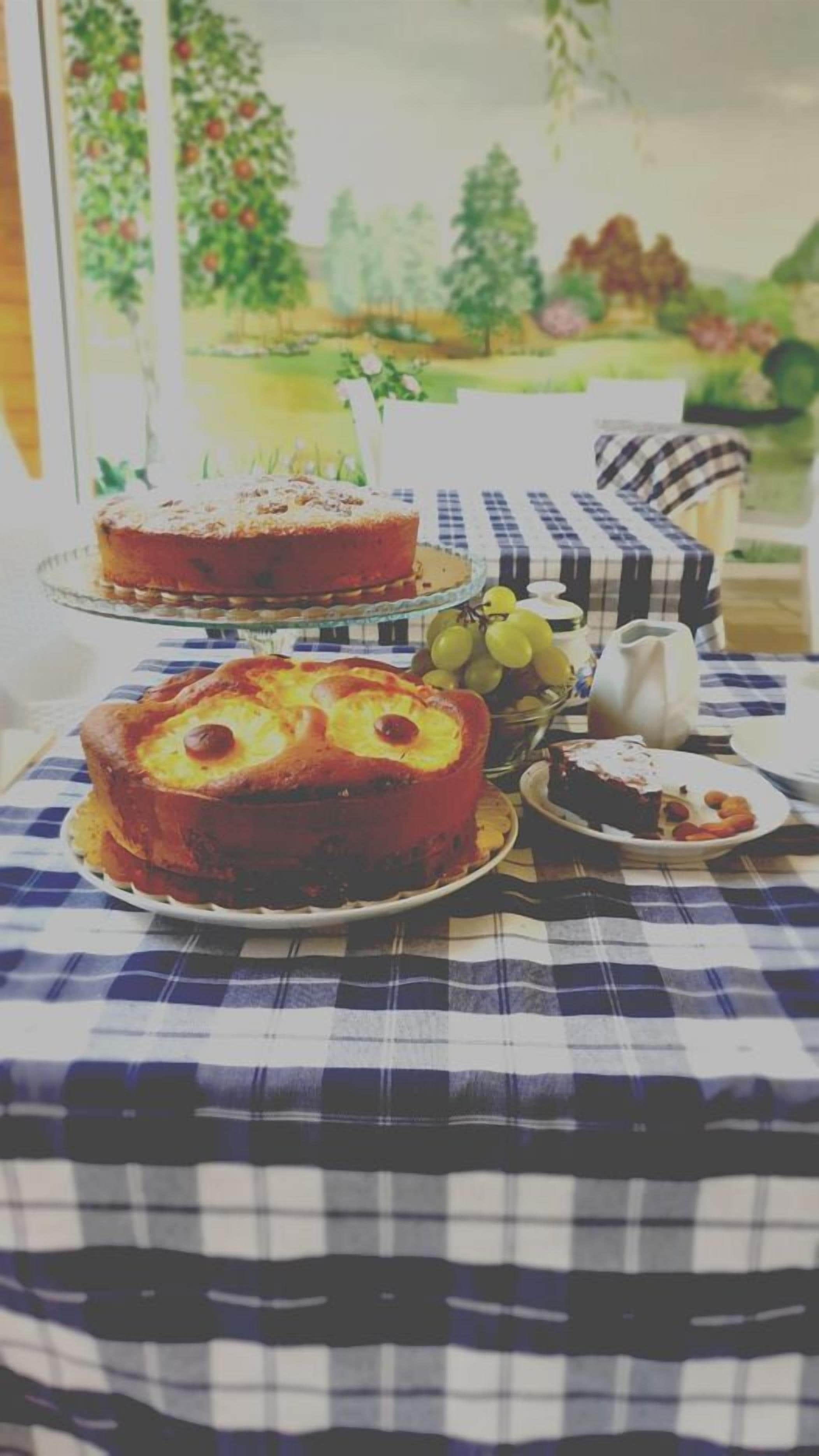 Una mesa con mantel a cuadros, un pastel decorado con piña, un plato de uvas y una tetera.