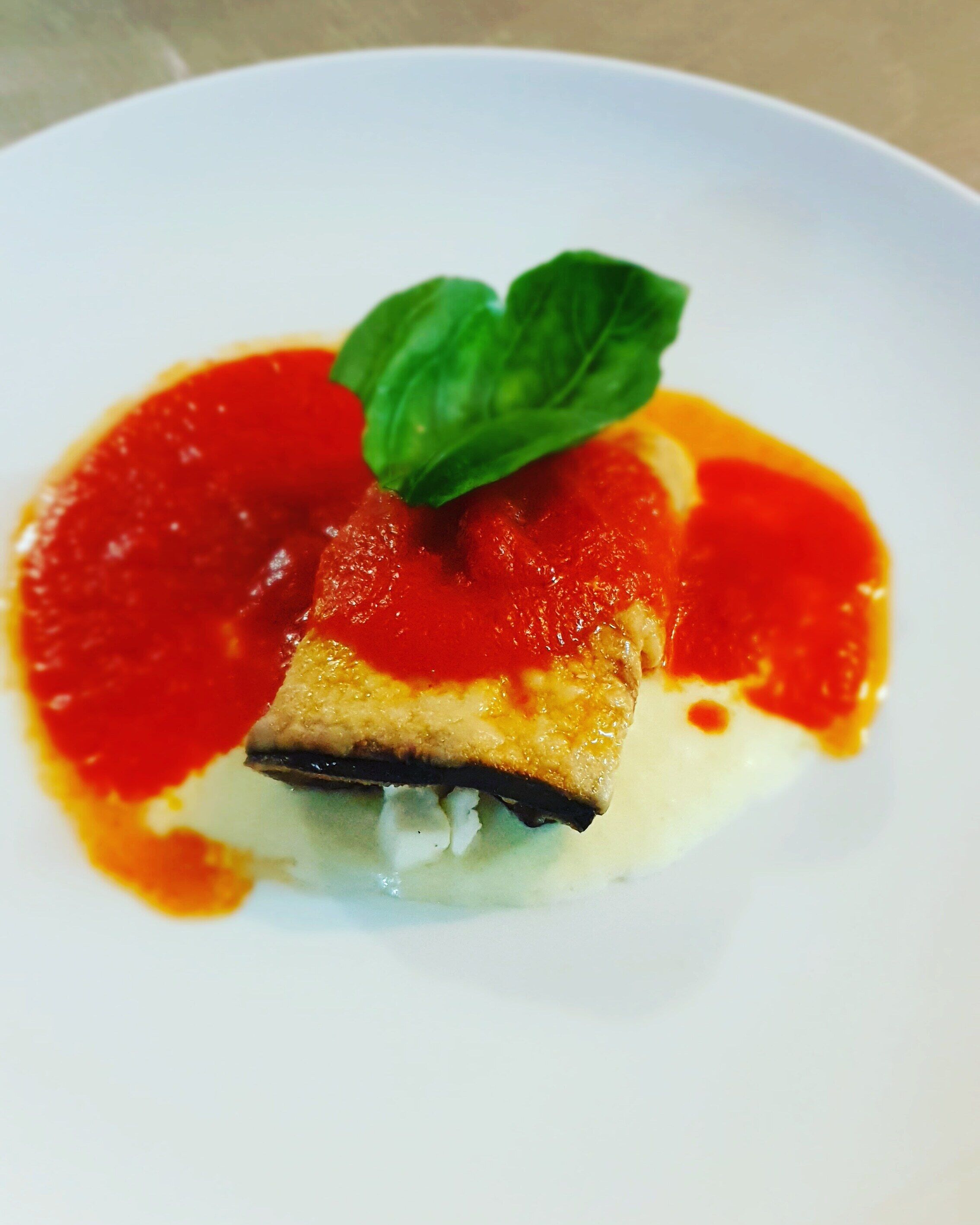 A plate with a slice of pizza topped with tomato sauce and a basil leaf.