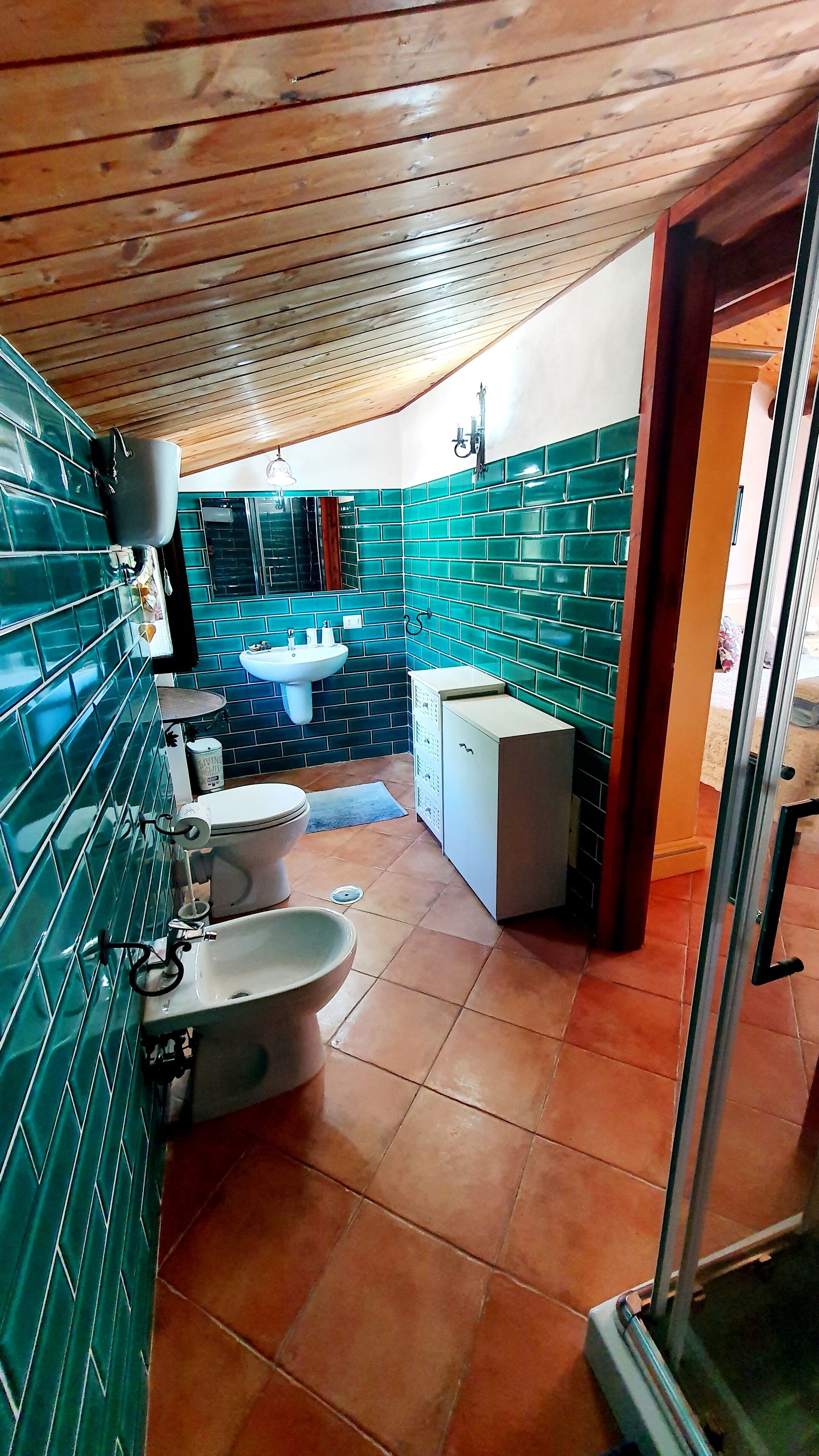 A compact bathroom with green-tiled walls, a white sink, and a toilet.