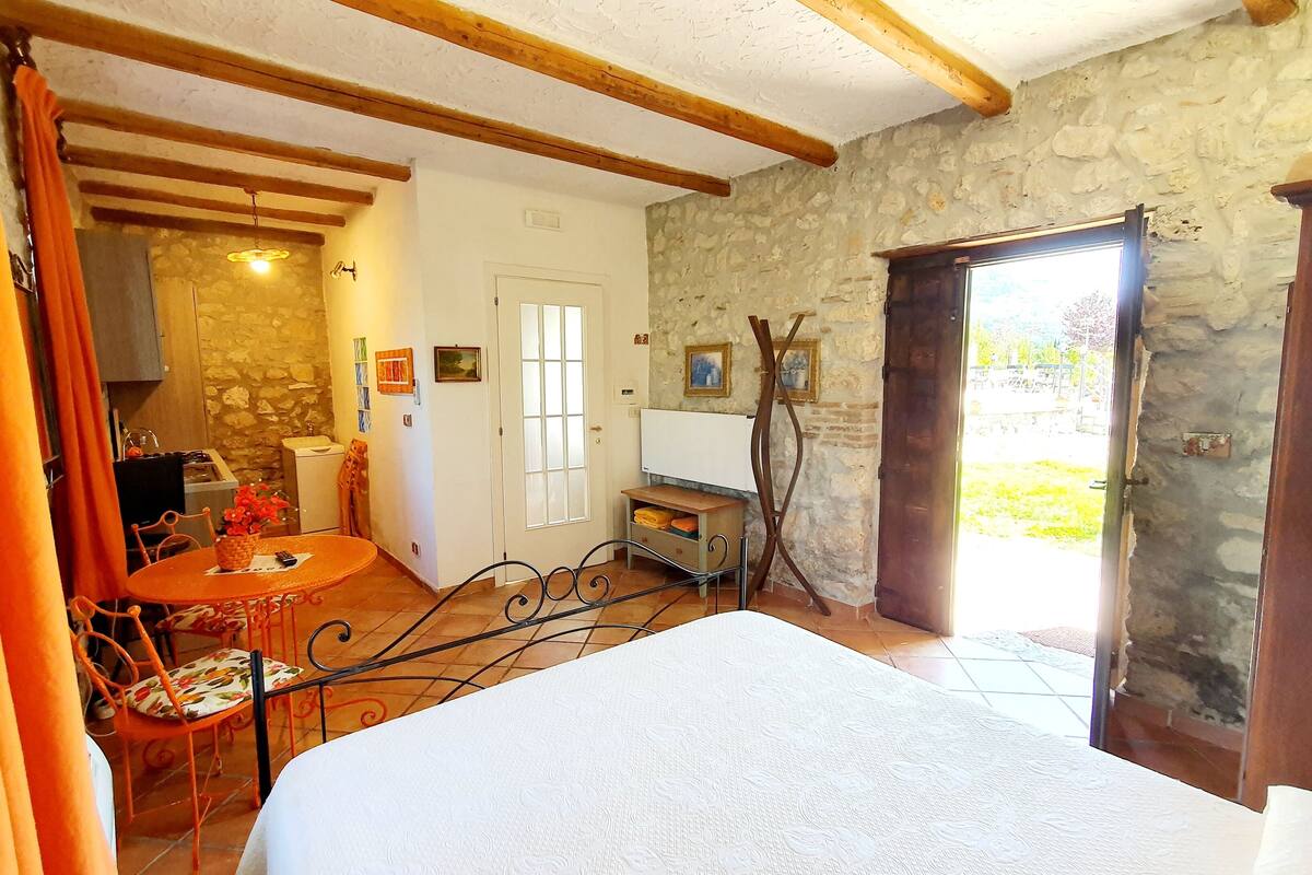 A room with a bed, a dining table with chairs, a kitchen area, and a stone wall.