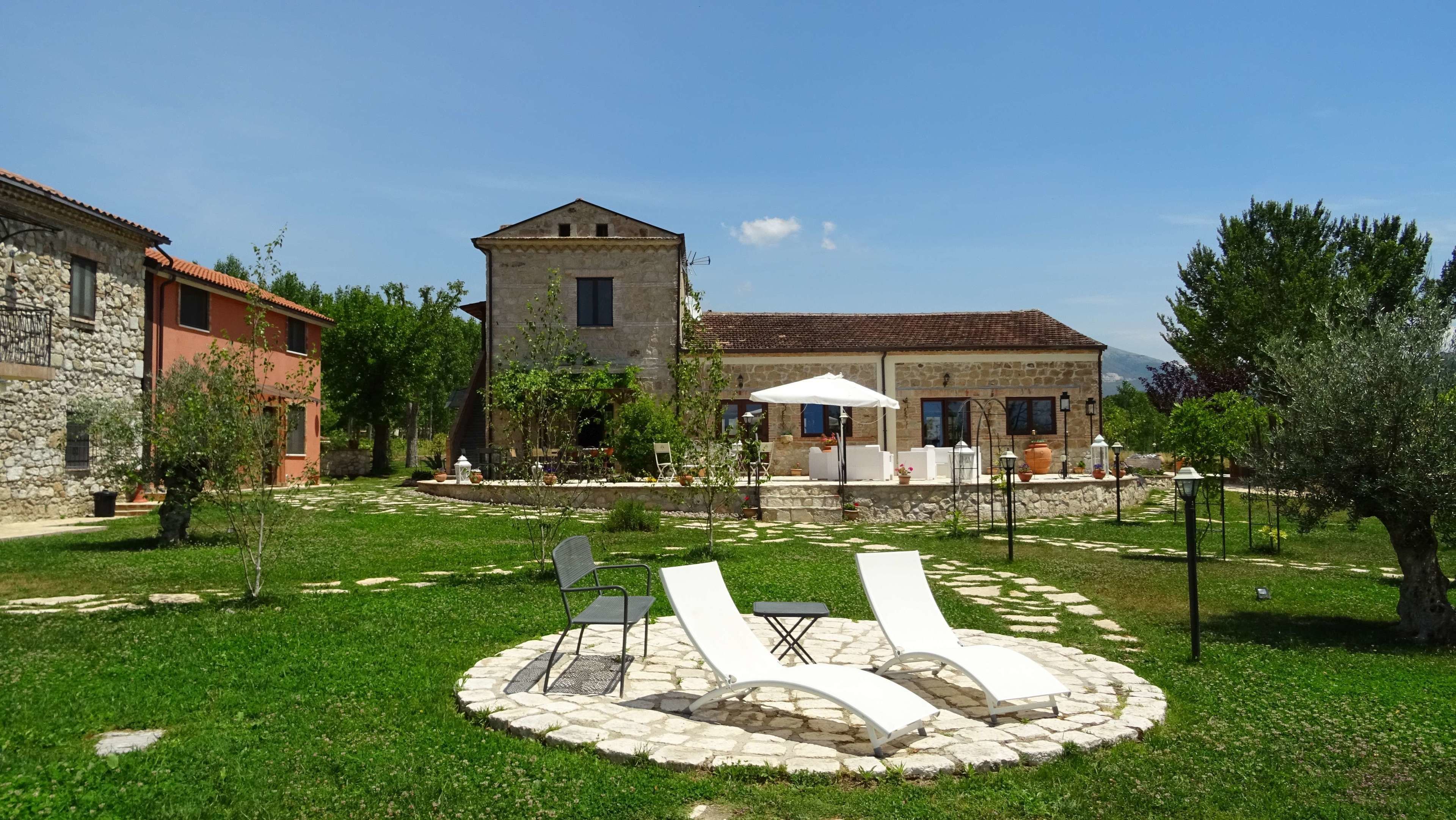 Un cortile con pavimento in pietra, posti a sedere all'aperto e un edificio in pietra con tetto in tegole.
