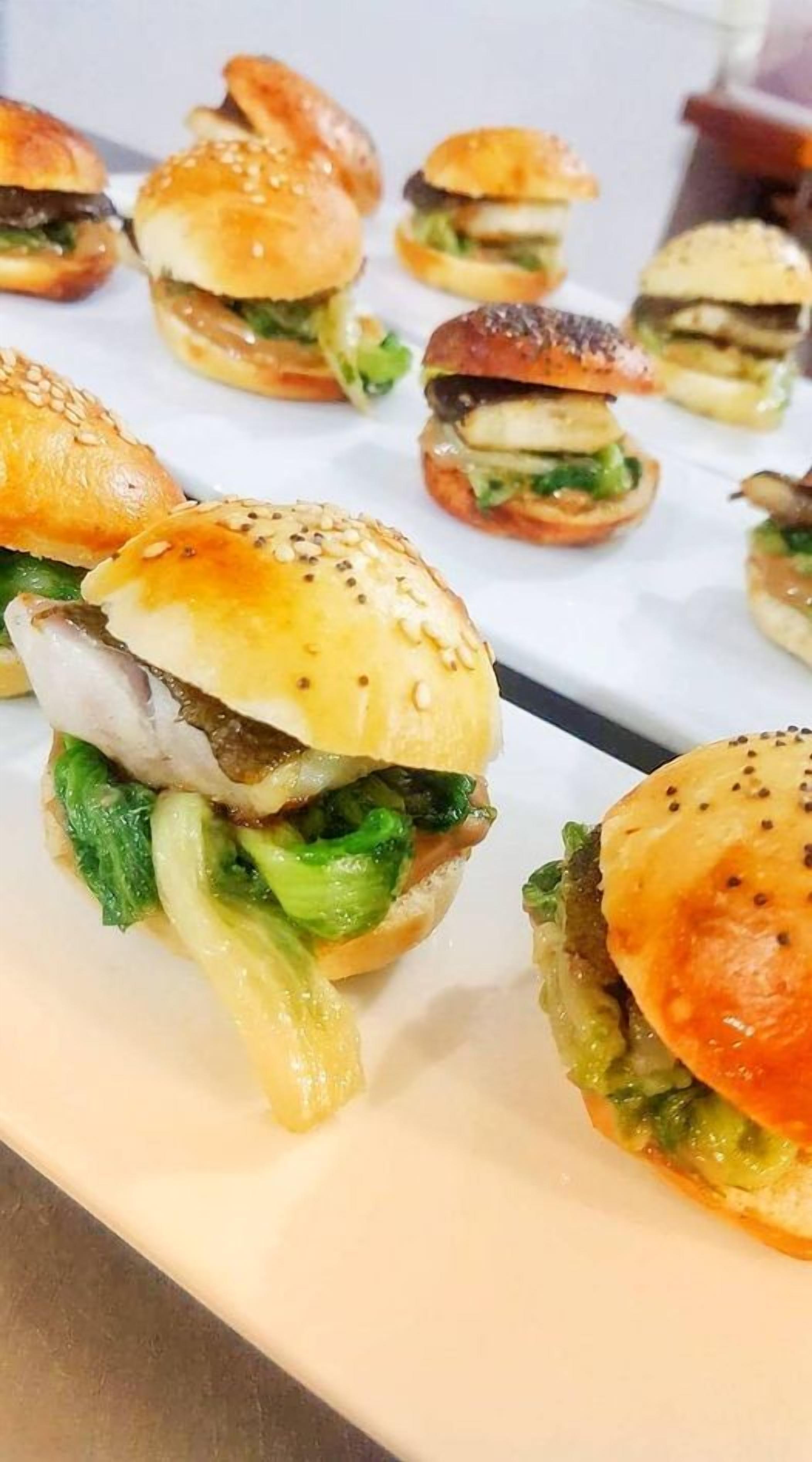 A tray of mini burgers with sesame seed buns and lettuce.