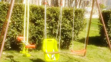 A swing set in a grassy yard with a house in the background.